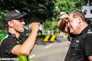 Policjant pije wodę z butelki, a drugi wyciera czoło.