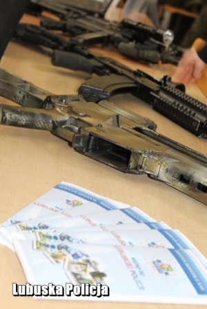 Ulotki profilaktyczne i broń na stole przy stoisku policyjnym.