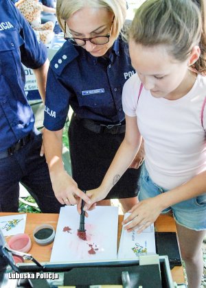 Policjantka prezentuje dziecku sposób zbierania śladów kryminalistycznych.