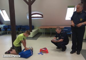 policjant i strażnik miejski uczą chłopca pierwszej pomocy