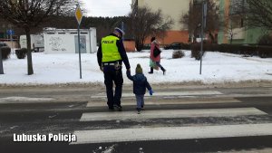 Policjant ruchu drogowego przeprowadza przez przejście dla pieszych małoletniego