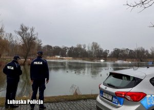 Umundurowani policjanci stoją nad brzegiem jeziora.