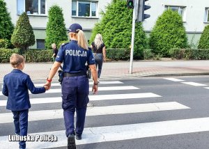 Policjantka idąca z chłopcem przez przejście dla pieszych.