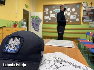Czapka policyjna i policjant w tle opowiadający dzieciom o bezpieczeństwie