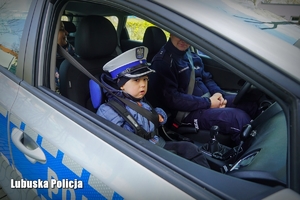 Mały chłopiec siedzący w radiowozie w towarzystwie policjanta.