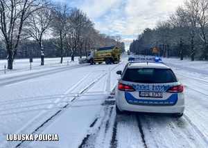 Policyjny radiowóz na zaśnieżonej drodze - w tle piaskarka.