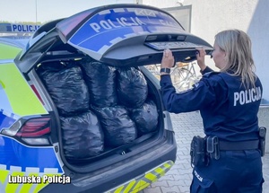 Policjantka zamyka klapę bagażnika radiowozu, w którym znajdują się worki pełne nakrętek.