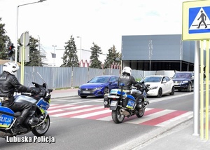 Policyjni motocykliści przejeżdżają po przejściu dla pieszych.
