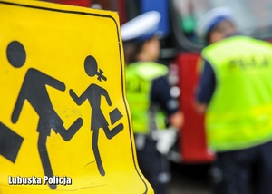 Znak dotyczący przewozu dzieci, a w tle policjanci drogówki.