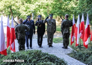 Funkcjonariusze służb mundurowych oddają hołd przed pomnikiem.