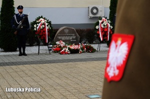 Godło Polski na żołnierskim mundurze, a w tle posterunek honorowy Policji przy pomniku.