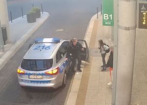 Policjantka otwiera drzwi od radiowozu przed dziewczynka na przystanku autobusowym.