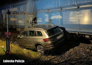 Uszkodzony pojazd osobowy stojący na nasypie kolejowym przy pociągu towarowym.