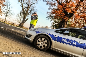 Policjant stojący z urządzeniem do pomiaru prędkości przed radiowozem