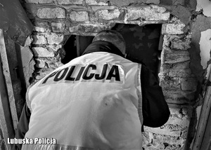 Czarno - białe zdjęcie - policjant sprawdzający miejsce przebywania osób bezdomnych.