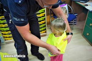 policjant ubiera dziecku kamizelkę odblaskową