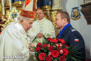 Komendant Wojewódzki Policji wręcza bukiet kwiatów biskupowi.