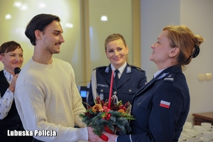 Młody mężczyzna wręcza prezent świąteczny policjantce.