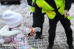Policjant wręcza element odblaskowy małej dziewczynce.