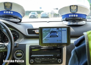 Widok na policyjny wideorejestrator, w tle widoczne czapki policjantów ruchu drogowego