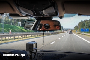 Odbicie policjanta prowadzącego radiowóz w lusterku środkowym pojazdu