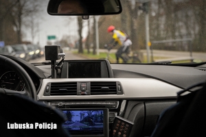 Widok z policyjnego radiowozu, w tle widoczny rowerzysta