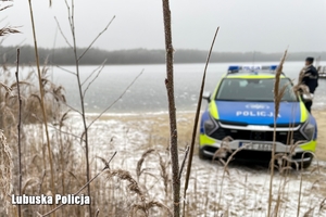 Policjant oraz radiowóz na tle zamarzniętego jeziora