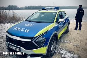 Policjant oraz radiowóz na tle zamarzniętego jeziora
