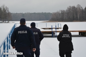 policjanci i strażniczka miejska obserwują zamarznięte jezioro