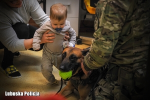 Kobieta trzymająca dziecko a obok policyjny pies służbowy