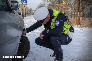 Policjant podczas kontroli drogowej sprawdza oponę pojazdu.
